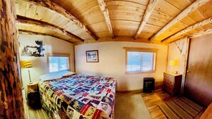 A cozy bedroom with a wooden ceiling, a bed with a patterned quilt, a nightstand with a lamp, and a window with blinds. - Great mountain cabin with river views. Sleeps 4. 15 miles to Wolf Creek Ski area and 3/4 mile private fishing. (South Fork)