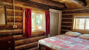 A log cabin bedroom with a bed, a dresser, and two windows with red curtains. - Mountain cabin with river views sleeps 8 . 15 minutes from Wolf Creek Ski Area. (South Fork)