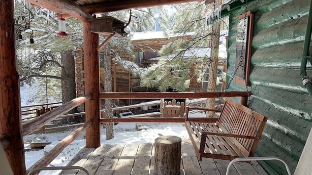 A wooden deck with a bench and chairs, a wooden table, and a view of trees and a building in the background. - Mountain cabin with river views sleeps 8 . 15 minutes from Wolf Creek Ski Area. (South Fork)