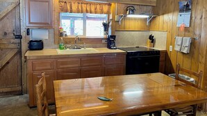 A rustic kitchen with wooden cabinets, a sink, a coffee maker, and a dining table. - Mountain cabin with river views sleeps 8 . 15 minutes from Wolf Creek Ski Area. (South Fork)