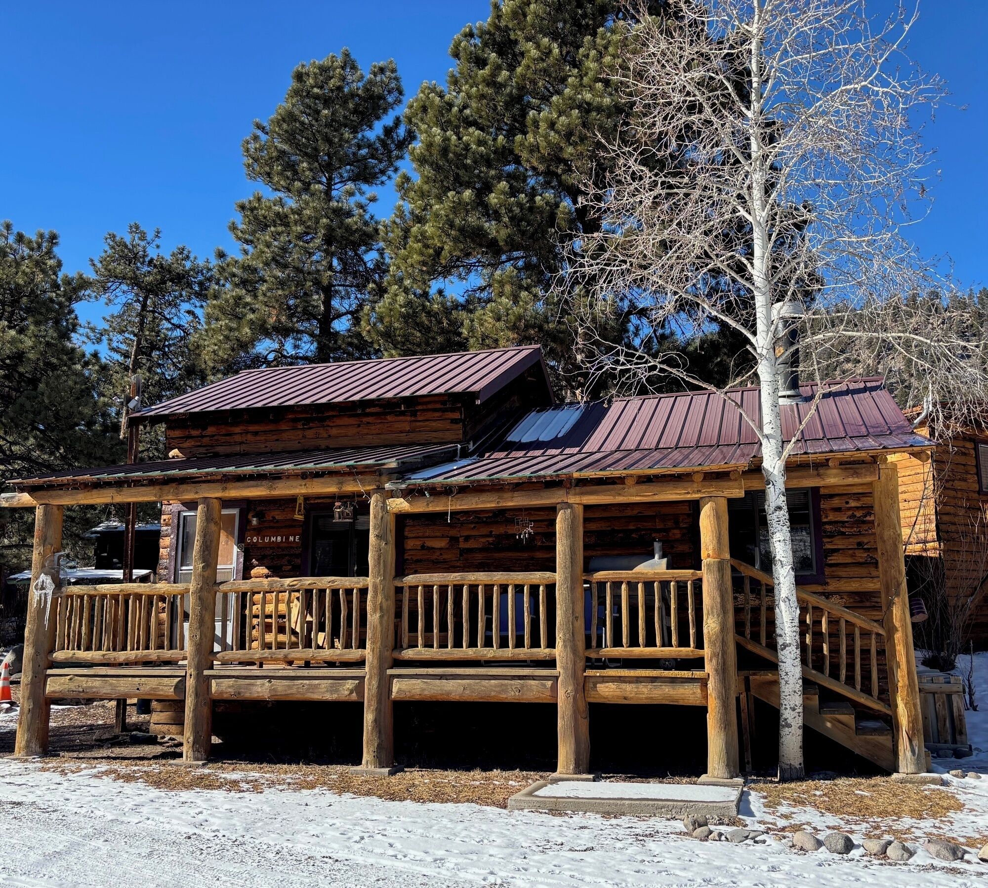 A wooden cabin with a metal roof, a wooden deck, and a staircase leading to the entrance.