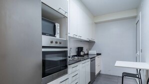 Una cocina compacta con armarios blancos, horno integrado, microondas, cafetera y una pequeña mesa de comedor con sillas.