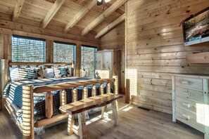 Une chambre dans un chalet en bois, avec un lit, un banc, une commode et un téléviseur fixé au mur.
