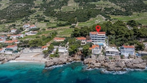 Vue aérienne d’une ville côtière avec des vignobles en terrasses, une plage et un hôtel doté d’un toit rouge.
