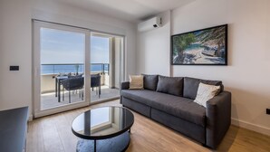 Un salon moderne avec un canapé gris, une table basse en verre et un balcon offrant une vue sur la mer.