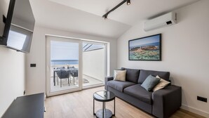 A modern living room with a grey sofa, a round coffee table, and a large window overlooking the sea. - Cozy apartment in Potomje with lake view (Potomje)