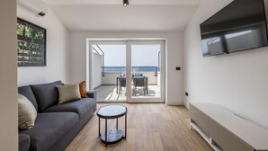 Ein modernes Wohnzimmer mit einem grauen Sofa, einem kleinen runden Tisch und einem an der Wand befestigten Fernseher.