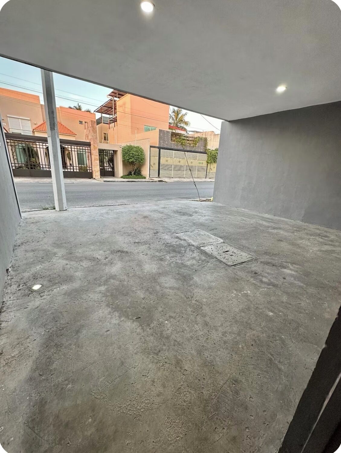 Une pièce vide avec un sol en béton, de grandes fenêtres et une vue sur une rue bordée d’immeubles.
