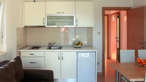 A compact kitchen with white cabinets, a built-in microwave, a sink, and a small refrigerator. There is a dining table with a bowl of fruit and a chair. - 1 bedroom awesome apartment in Klek (Klek)