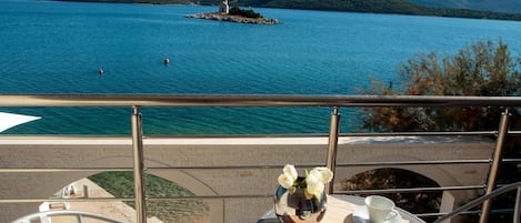 A balcony with a table set for two, overlooking a lake with a small island and mountains in the distance.