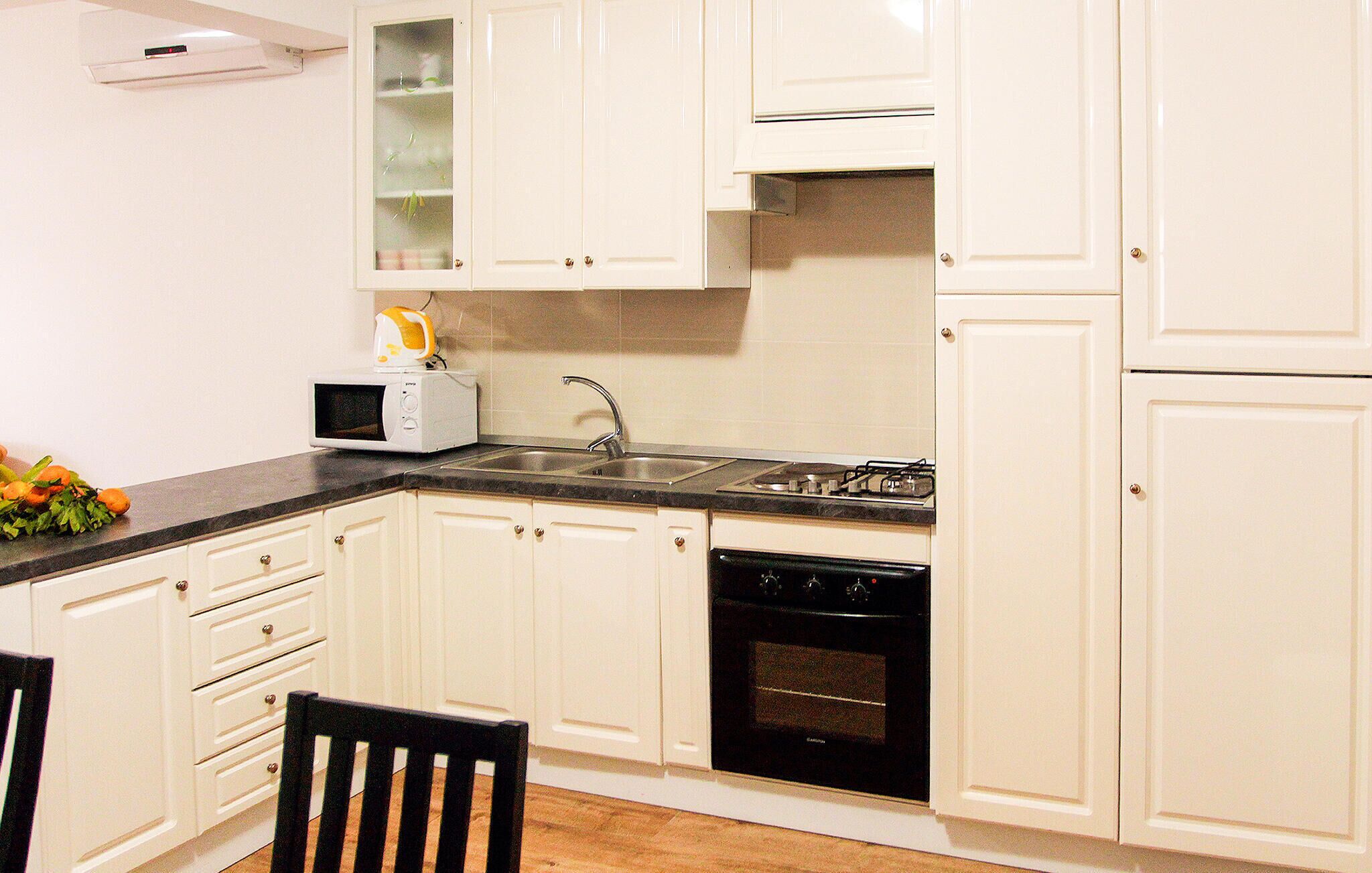A kitchen with white cabinets, a black countertop, a microwave, a sink, and a stove.