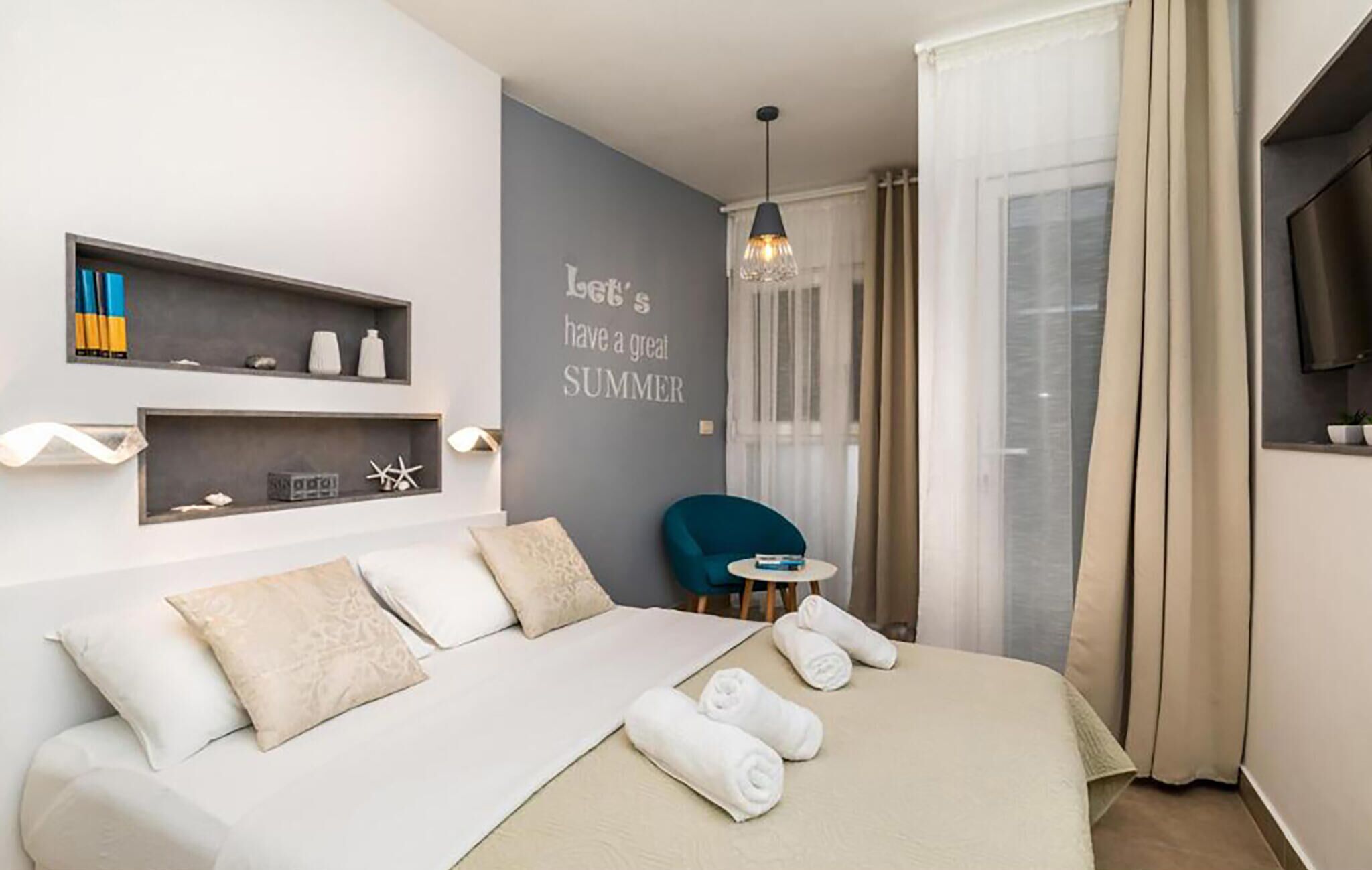 A modern hotel room with a bed, a small table, a chair, and a wall with a motivational quote.
