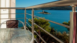 A balcony with a metal railing overlooking a body of water, a small island with a structure, and a wicker chair. - Amazing apartment in Klek with WiFi (Klek)