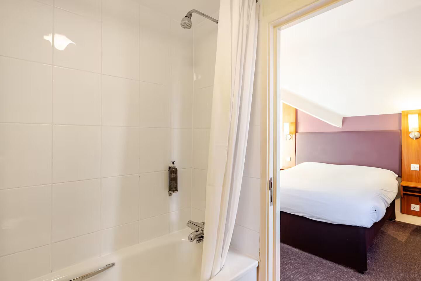 A hotel room with a shower, a bed, and a nightstand with a lamp.