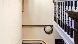 En smal trappa med ett mörkt heltäckningsmatta, en vit vägg och ett svart räcke med en rund spegel högst upp.