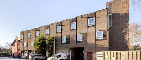 Un edificio residencial de varios pisos con fachada de ladrillo, múltiples ventanas y una entrada protegida por un portón.