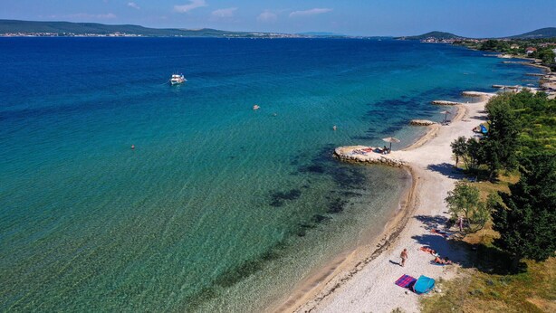 Una playa costera con aguas cristalinas, un bote y gente tomando el sol.