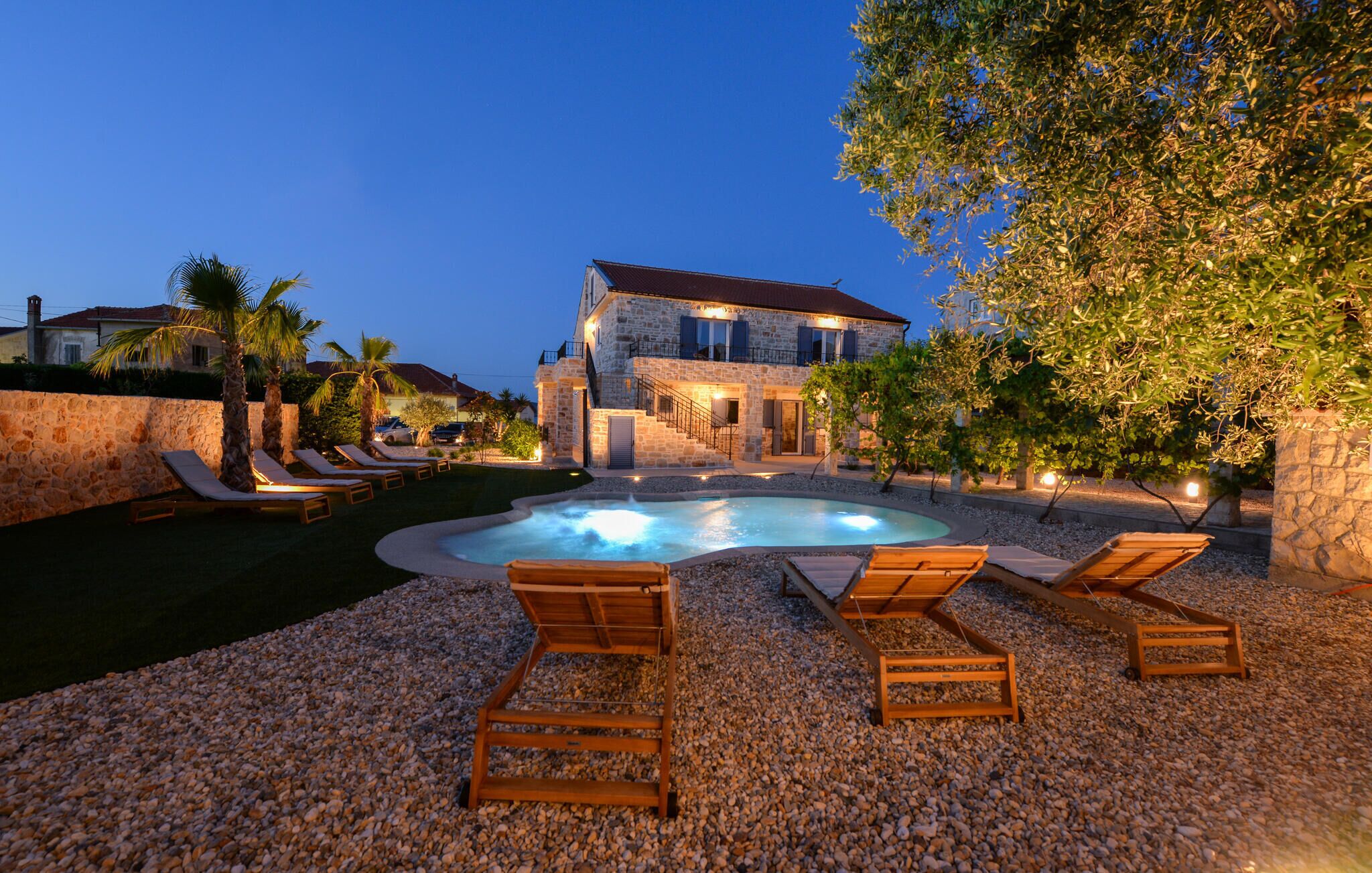 A stone villa with a swimming pool, lounge chairs, and a well-lit outdoor area.