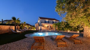 Una villa de piedra con piscina, sillones de descanso y un área exterior bien iluminada.