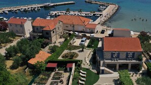 Una propiedad costera con un puerto deportivo, varios edificios con tejados rojos y un jardín ajardinado con tumbonas.