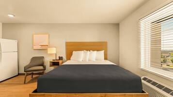 A hotel room with a bed, a chair, a desk with a lamp, and a window with blinds.