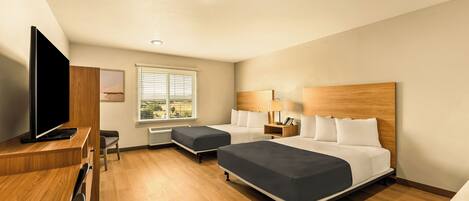 A hotel room with two beds, a desk with a TV, a window with blinds, and a wooden headboard.