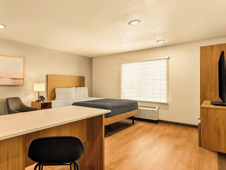 Een kleine hotelkamer met een bed, bureau, stoel en een televisie op een houten kast.