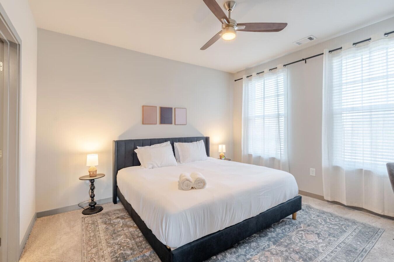Une chambre d’hôtel avec un lit, deux tables de chevet, un ventilateur de plafond et une grande fenêtre avec des rideaux.