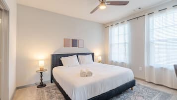Une chambre d’hôtel avec un lit, deux tables de chevet, un ventilateur de plafond et une grande fenêtre avec des rideaux.