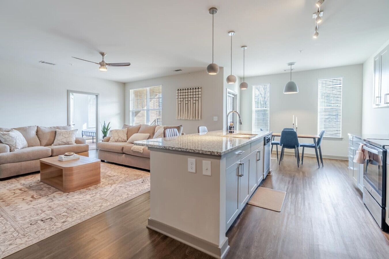 A modern kitchen with a central island, a dining area with a table and chairs, and a living room with a sofa and coffee table.