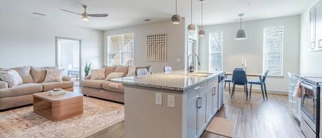 A modern kitchen with a central island, a dining area with a table and chairs, and a living room with a sofa and coffee table.