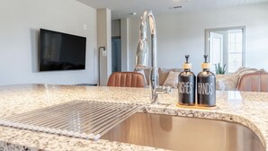 Una cocina con encimera de granito, grifo de acero inoxidable y dos botellas con la etiqueta 'DISHES' y 'HANDS'.