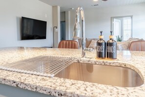 A kitchen with a granite countertop, stainless steel faucet, and two bottles labeled 'DISHES' and 'HANDS'. - Bright, Cozy 3BD Apt w/ Pool + Gym (Matthews)