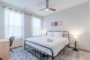 A bedroom with a bed, bedside lamps, a ceiling fan, and a desk.
