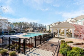 A pool area with a gazebo, surrounded by a fence, and adjacent buildings. - Bright & Elegant 1BD Abode w/ Pool & Gym (Matthews)