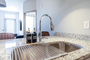 A kitchen with a granite countertop, stainless steel sink, and two black bottles labeled 'HAND DISHES'. - Bright & Elegant 1BD Abode w/ Pool & Gym (Matthews)