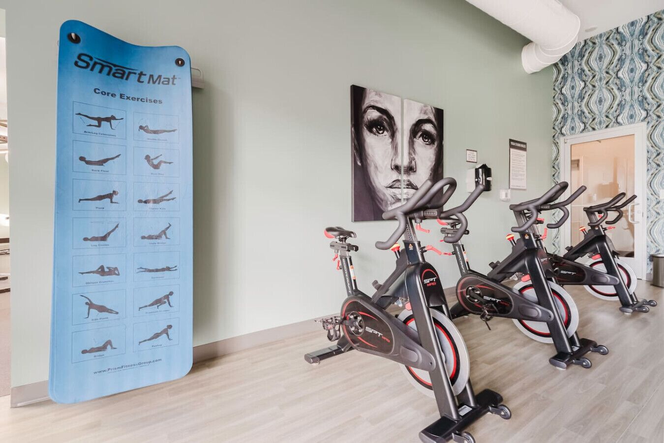 Ein Fitnessbereich mit Ergometer und einem SmartMat-Poster, das Übungen für die Körpermitte zeigt.