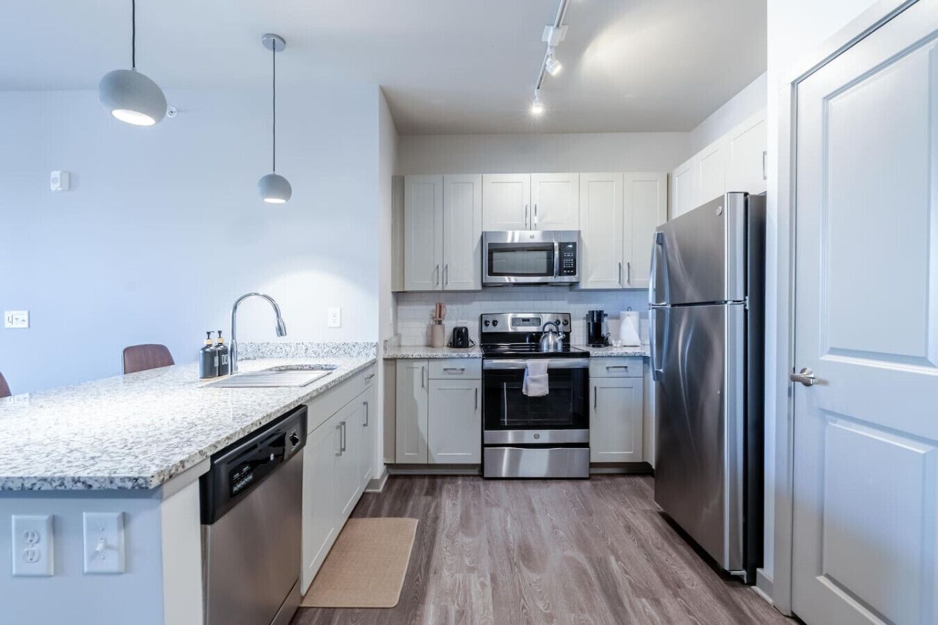 A modern kitchen with white cabinets, stainless steel appliances, a granite countertop, and pendant lighting.