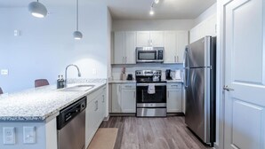 Una cocina moderna con armarios blancos, electrodomésticos de acero inoxidable, encimera de granito e iluminación colgante.