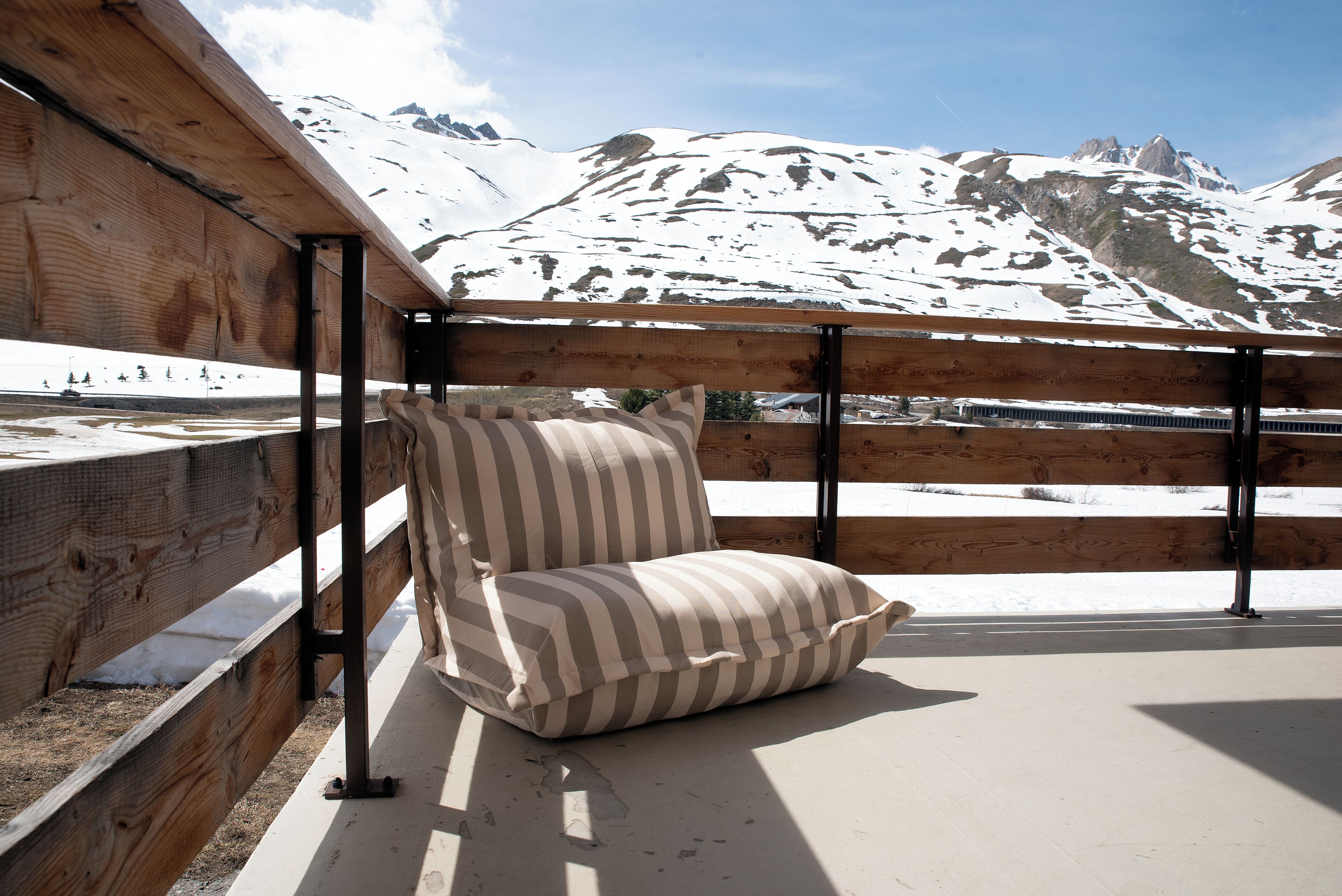 Een houten terras met een gestreepte stoel en uitzicht op besneeuwde bergen.