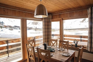 Ein Holzespeise-Tisch mit Stühlen, eine Pendelleuchte und Blick auf eine verschneite Landschaft durch große Fenster.