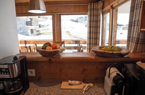 Une cuisine avec des plans de travail en bois, une machine à café et une fenêtre donnant sur des immeubles et un paysage enneigé.