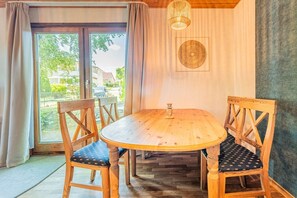 A wooden dining table with four chairs, a chandelier, and a view through a glass door. - Binzer Waldhof - Haus Fuchsbau (Binz)