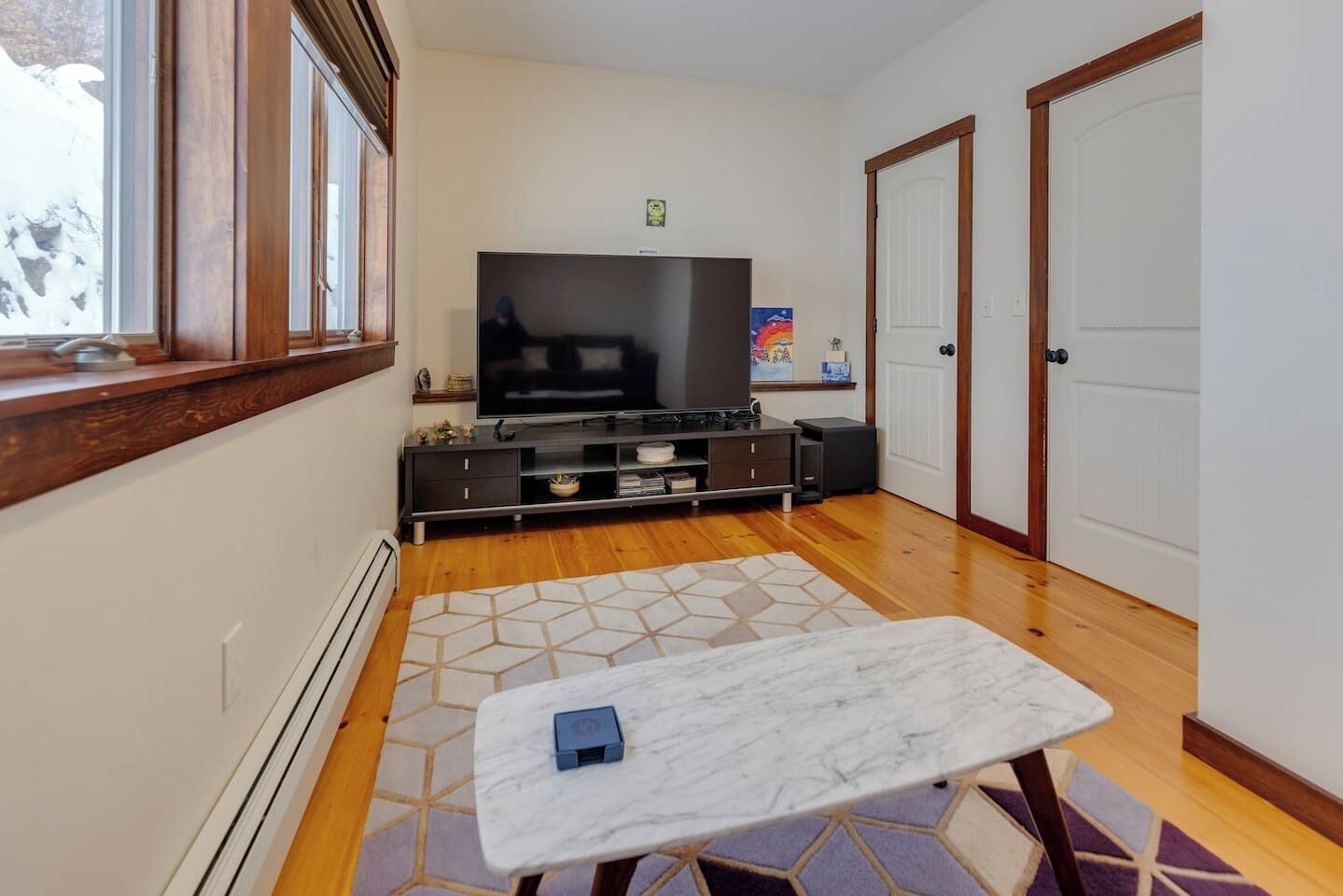 Una sala de estar moderna con un televisor de pantalla plana grande, piso de madera, una mesa de centro de mármol y una alfombra estampada.