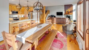 A modern kitchen with wooden cabinets, a central island, and a dining area with a wooden table and benches. - Coolidge Falls Retreat at Loon Mountain (Lincoln)