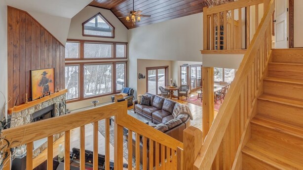 A spacious living area with a fireplace, a wooden staircase, and large windows offering views of the outdoors. - Coolidge Falls Retreat at Loon Mountain (Lincoln)