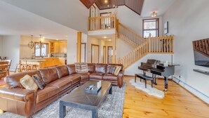 A spacious living area with a leather sectional sofa, a piano, and a wooden staircase. - Coolidge Falls Retreat at Loon Mountain (Lincoln)