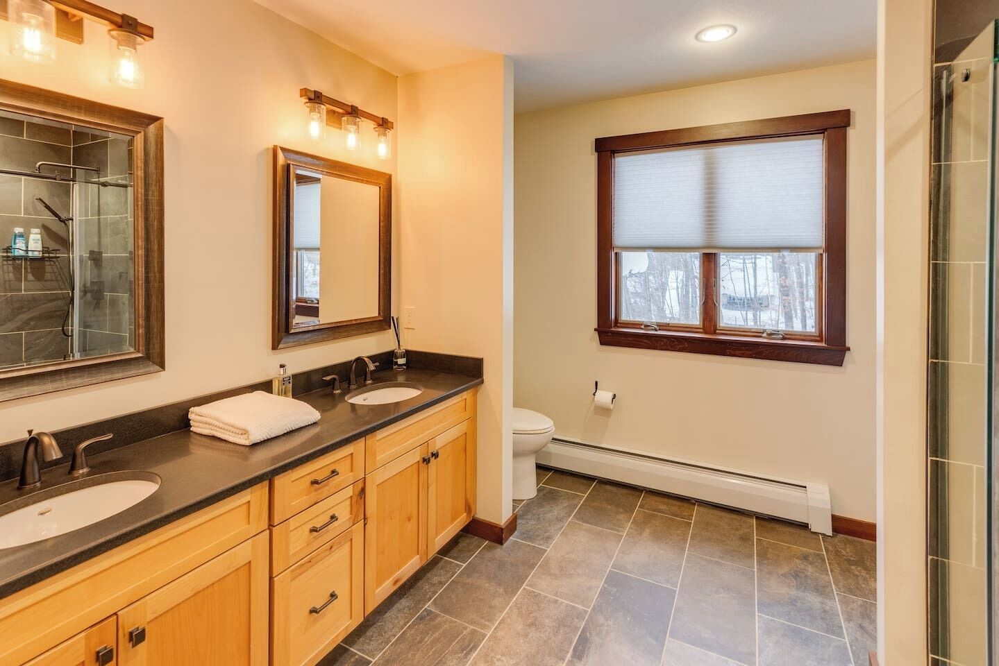 A bathroom with two sinks, a toilet, and a window.