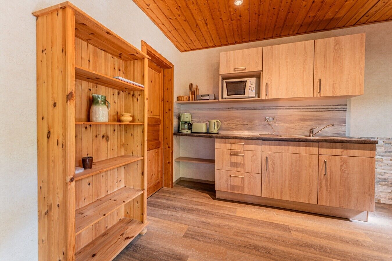 Un interior de madera con área de cocina, que incluye armarios, un microondas y una cafetera.