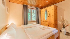 A bedroom with a wooden ceiling, a large window with curtains, a wardrobe, and a bed with towels. - Binzer Waldhof - Igelhaus (Binz)